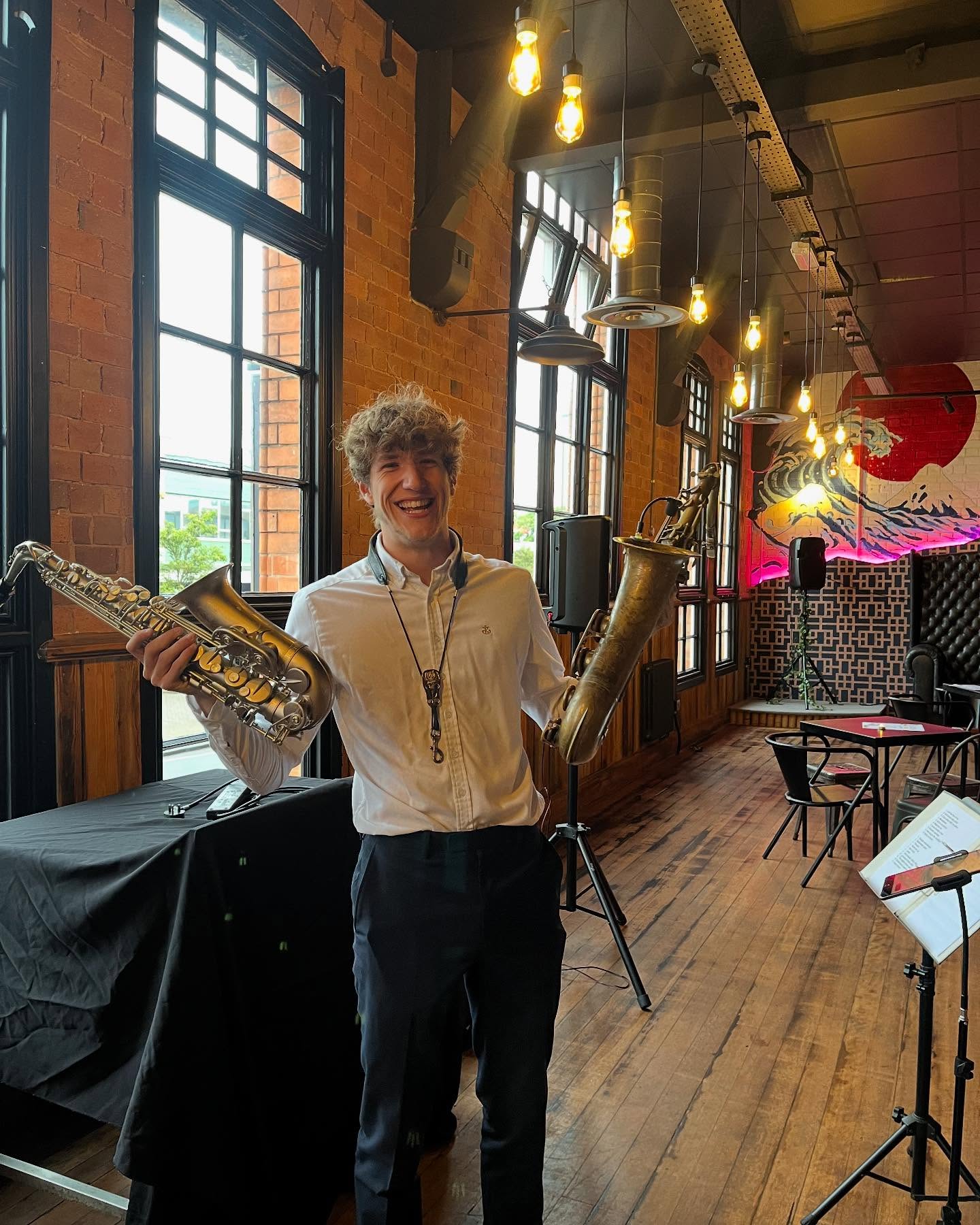 Me holding an alto and a tenor saxophone in a brick-walled bar